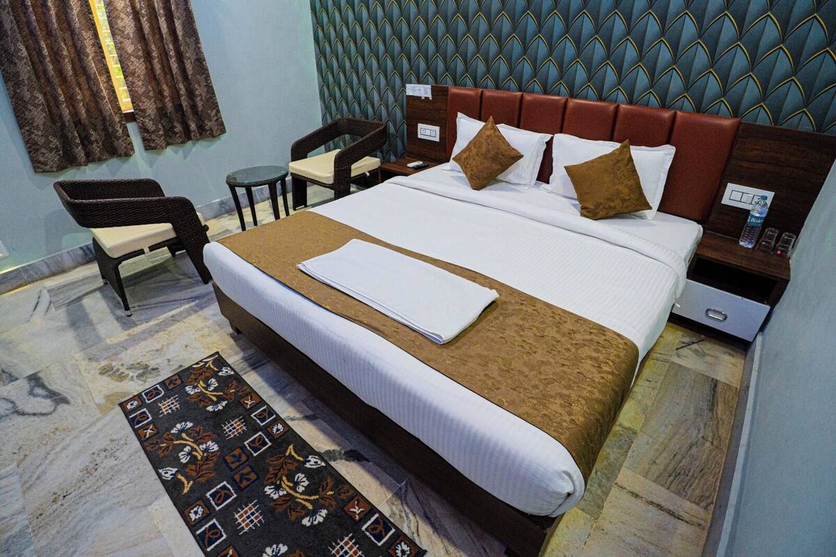 A hotel room with a large bed, a small table, a chair, a nightstand, and a patterned rug.