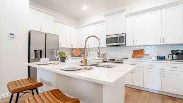A modern kitchen with white cabinetry, stainless steel appliances, and a central island with seating. - Game Day Home Base | Steps to Globe Life & AT&T (Arlington)