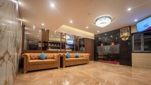 Eine moderne Lobby mit Marmorboden, zwei blauen Sofas, einem Kronleuchter und einem an der Wand befestigten Fernseher.