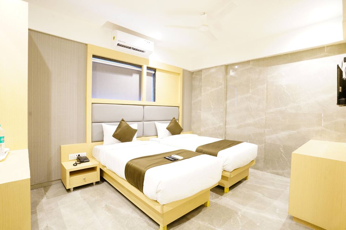 A hotel room with two beds, a bedside table with a phone, a small drawer, a wall-mounted TV, and a ceiling fan.
