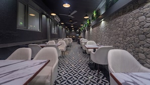 Ein Restaurant mit modernem Interieur, das einen gemusterten Boden, weiße Stühle und eine Steinwand zeigt.