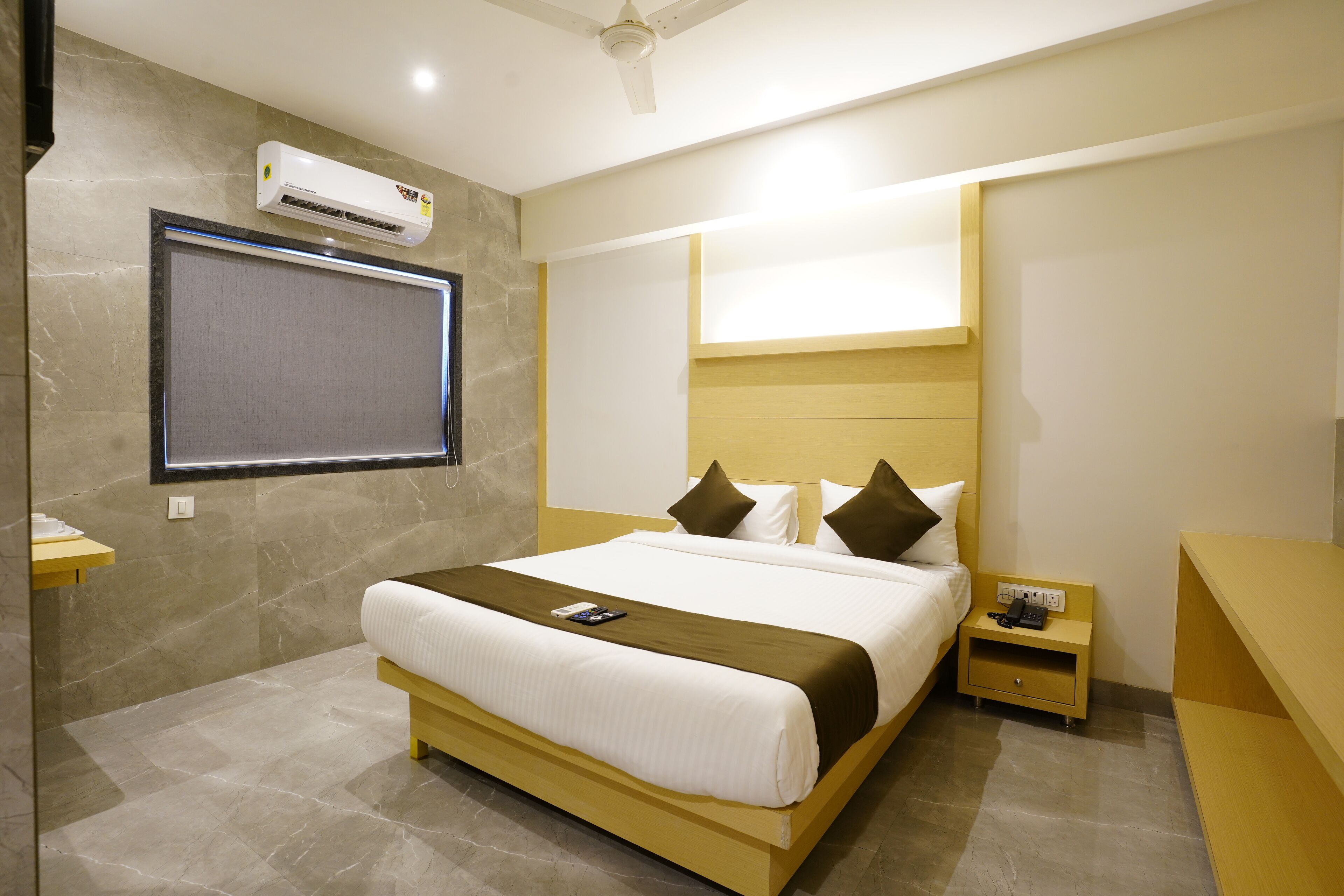 A modern hotel room with a large bed, a bedside table with a phone, and an air conditioning unit mounted on the wall.