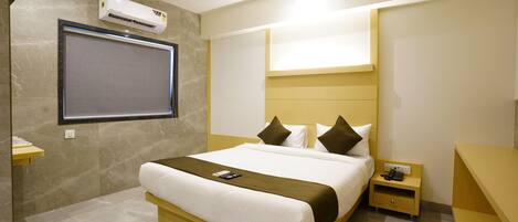 A modern hotel room with a large bed, a bedside table with a phone, and an air conditioning unit mounted on the wall.