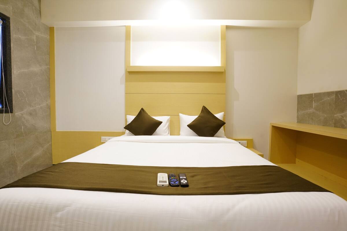 A hotel room with a large bed, two pillows, a bedside table, and a nightstand.