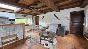A rustic interior with a stone-tiled floor, wooden ceiling beams, a dining area with white furniture, a sofa with a patterned throw, and a door with a decorative handle. - Farmhouse in Belgium With Lush Garden Retreat (Hastiere)