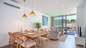 A modern living room with a dining area, large windows, and a view of a building complex. - A. Mirador Blue K Cala Sant Vicenç (Cala Sant Vicenç)
