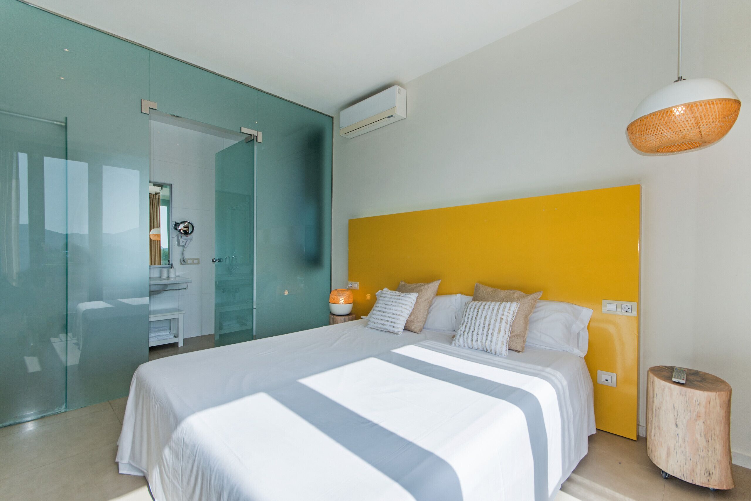 Een moderne hotelkamer met een groot bed, een glazen scheidingswand, een badkamer en een heldergele accentmuur.