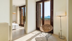 A balcony with a wicker chair, a floor lamp, and a view of the mountains.