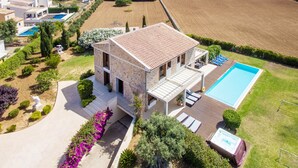 A two-story stone house with a swimming pool, outdoor seating, and a view of the sea and fields.