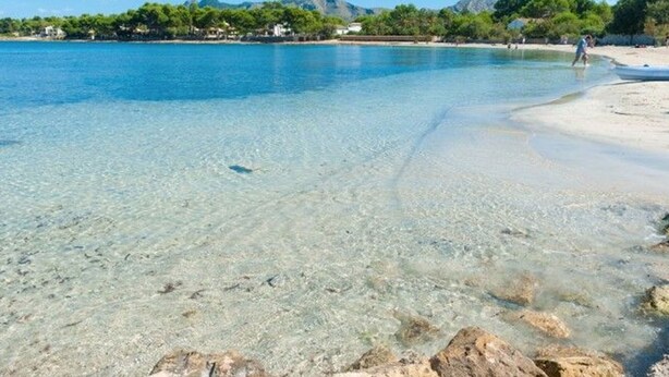 A clear beach with visible rocks and a few people.