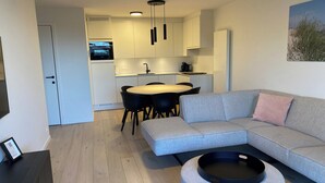 A modern living room with a grey sofa, a round ottoman, and a dining area with a table and chairs. - Apartment Near Marina Nieuwpoort & Pool (Nieuwpoort)