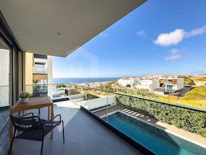 Ein Balkon mit Pool, Tisch und Stühlen mit Blick auf eine Küstenstadt.