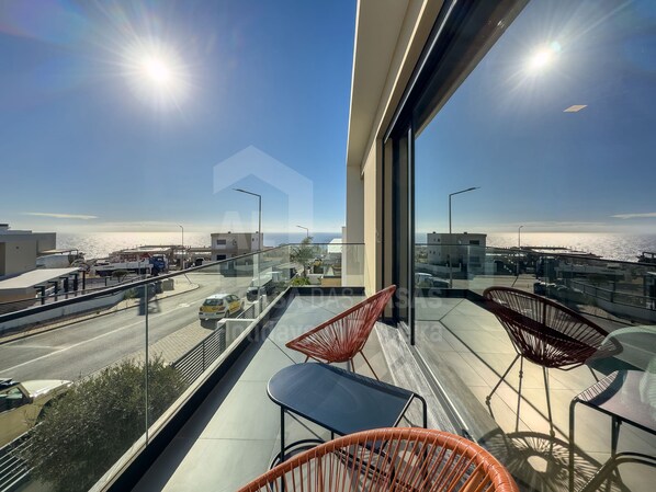 A balcony with a view of the sea, featuring outdoor furniture and a glass railing.