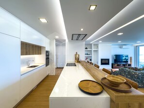 Una cocina moderna con una isla central grande, electrodomésticos integrados y un comedor con televisor y asientos.