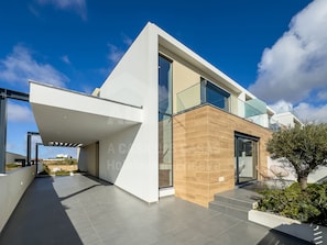 Ein modernes, zweistöckiges Haus mit Flachdach, großen Fenstern und einer überdachten Terrasse.