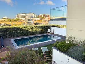 Una piscina en la azotea con vistas a edificios residenciales, rodeada de vegetación y mobiliario de exterior.