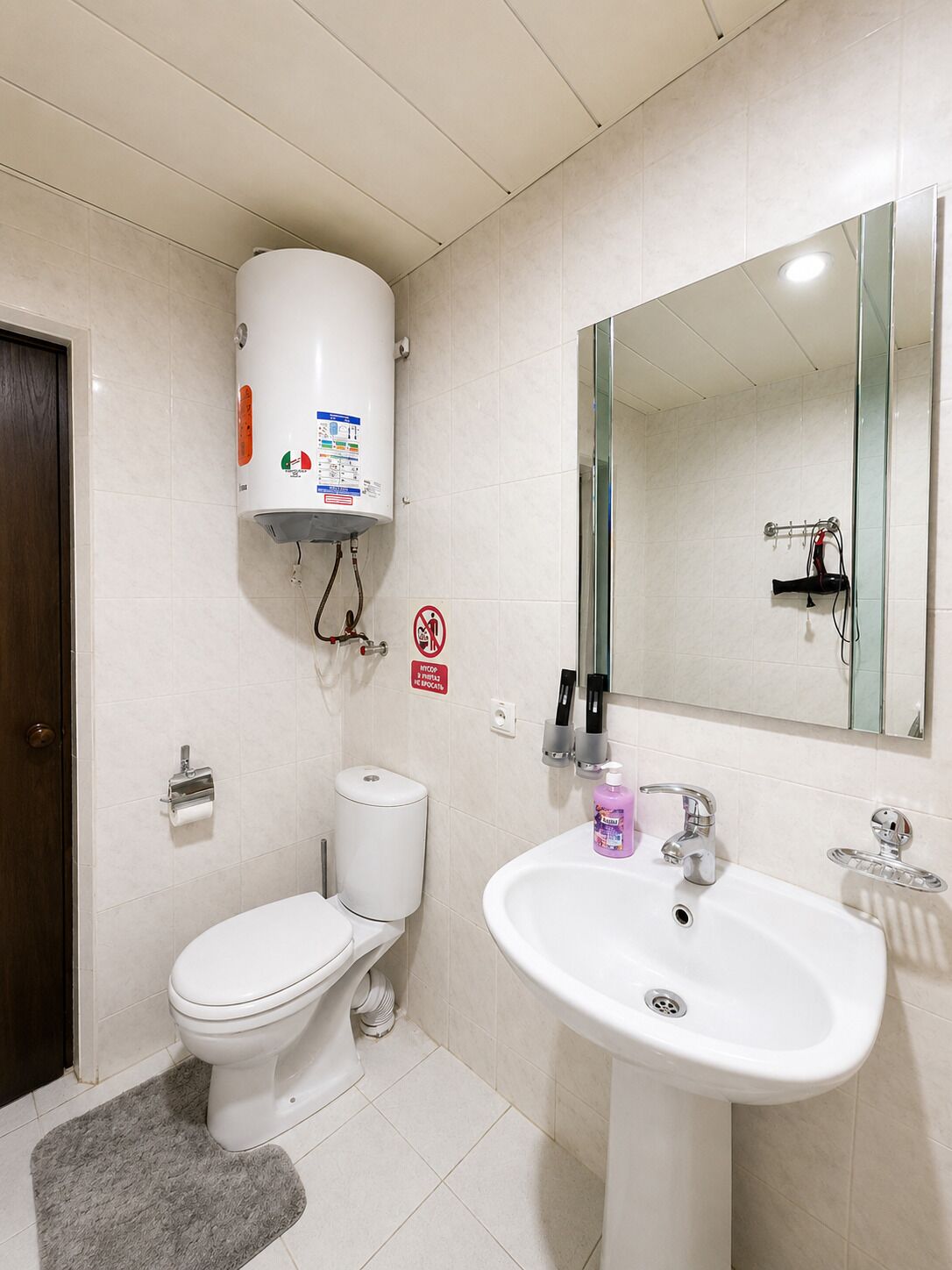 Une salle de bain équipée de toilettes, d’un lavabo, d’un miroir et d’un chauffe-eau.