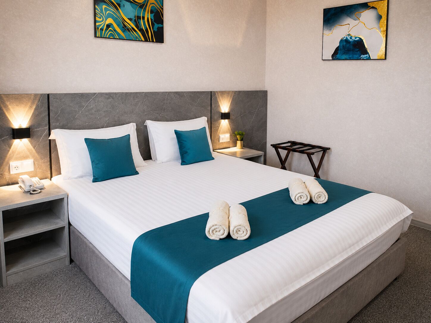 A hotel room with a large bed, two bedside tables, a wall-mounted phone, and two wall-mounted lamps.