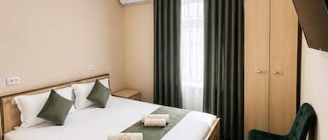 A hotel room with a bed, a desk, a chair, a TV, and an air conditioning unit.
