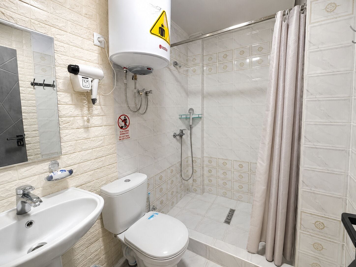 Un baño con inodoro, lavamanos, ducha y un perchero para toallas.