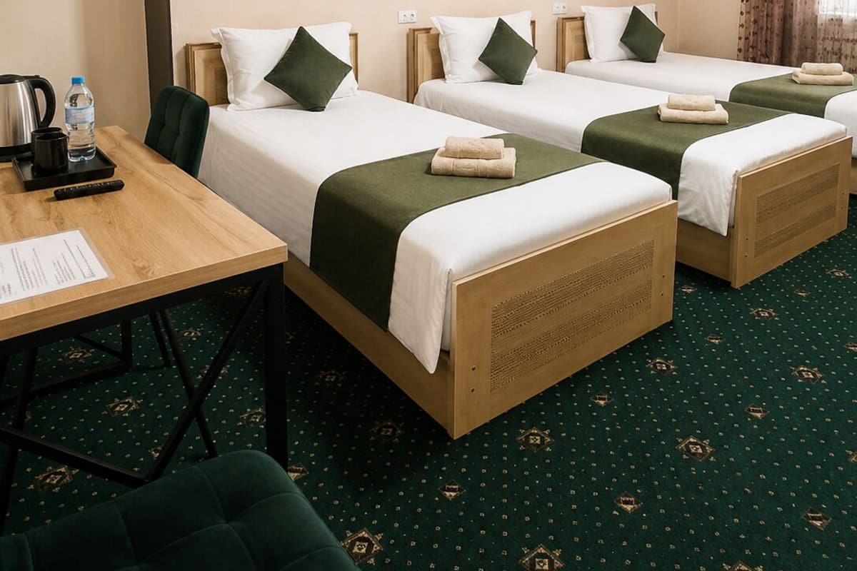 Une chambre d’hôtel avec trois lits, un bureau, une chaise et un porte-manteau.