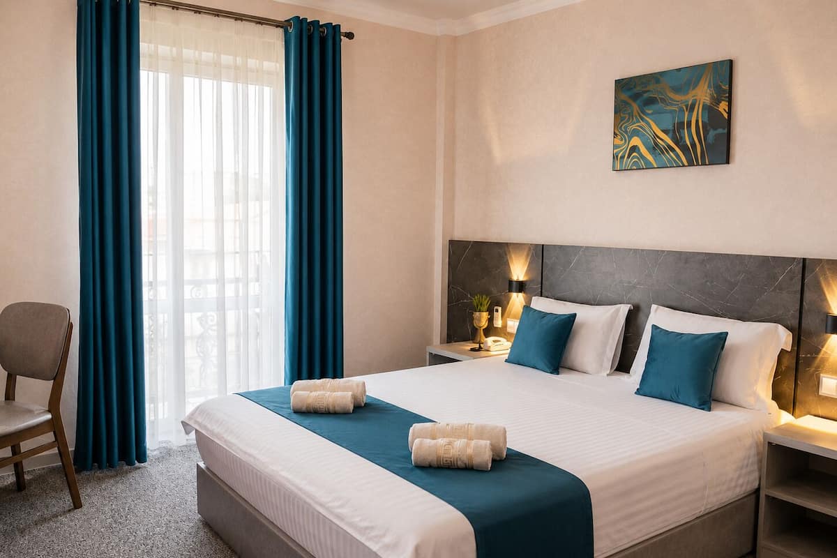 Une chambre d’hôtel avec un grand lit, deux tables de chevet, une chaise, un tableau au mur et une fenêtre avec des rideaux.