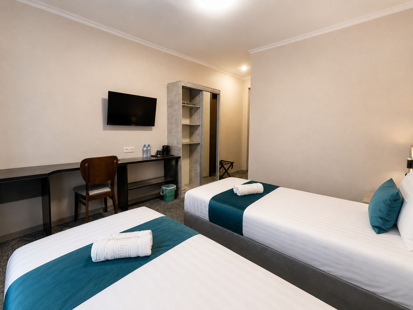 Ett hotellrum med två sängar, ett skrivbord, en stol, en TV och en garderob.