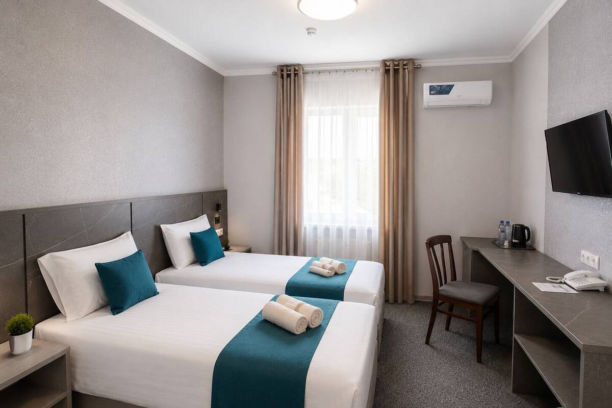 Une chambre d’hôtel avec deux lits, un bureau, une chaise, une télévision et une fenêtre avec des rideaux.