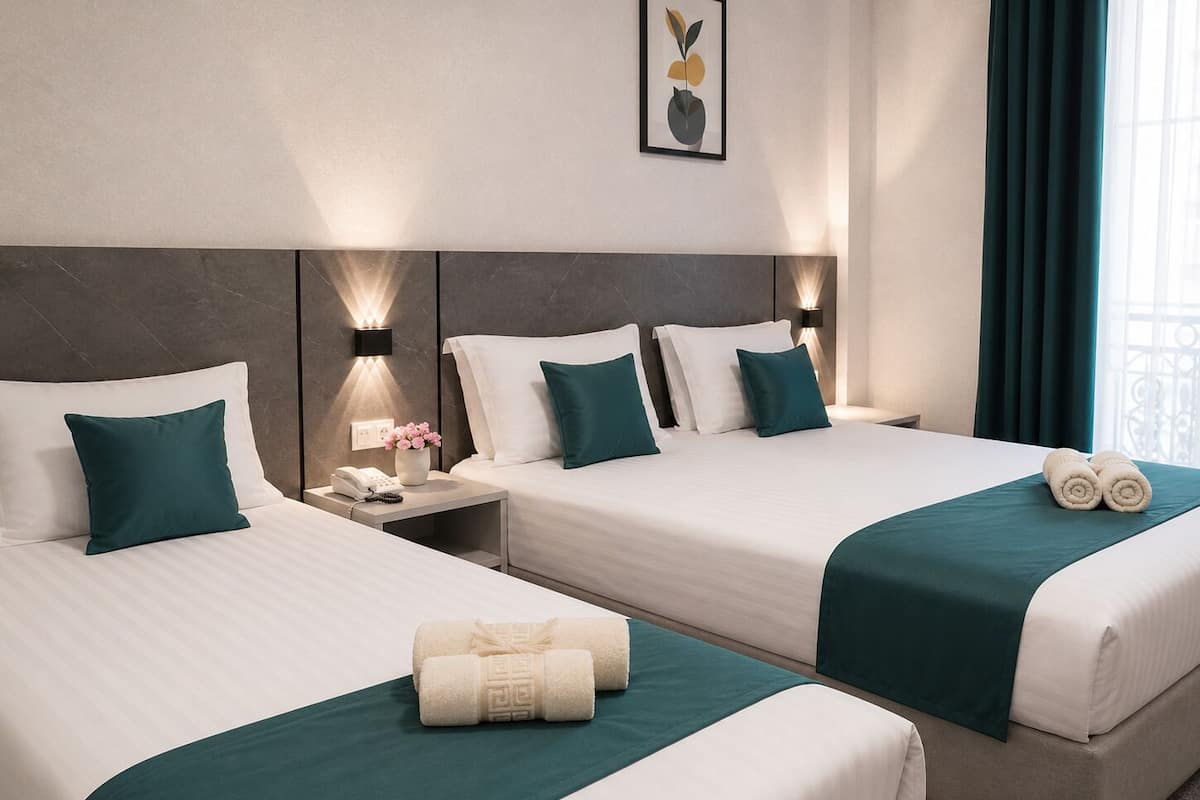 Une chambre d’hôtel avec deux lits, chacun agrémenté de draps blancs et de touches de couleur turquoise, une table de chevet avec un téléphone et un vase, et un tableau encadré au mur.