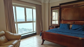 Um quarto com uma cama grande, um sofá de couro e vista para o mar através de janelas amplas.
