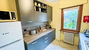 Eine kleine Küche mit einem Kühlschrank von Bosch, grauen Schränken, einer Holz Arbeitsplatte und einem Fenster mit Blick auf Grünflächen.