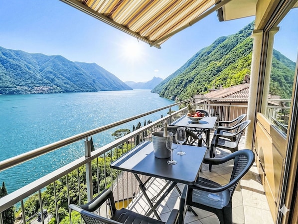 A balcony with a table, chairs, and a view of a lake and mountains.