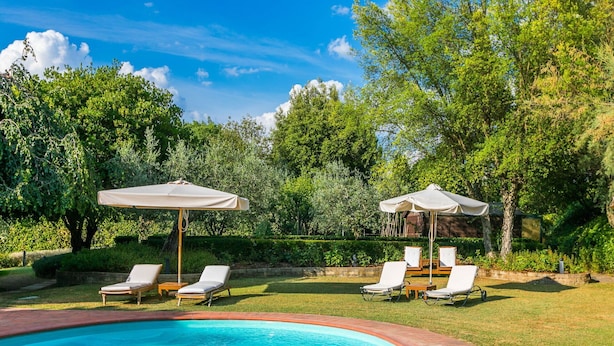 Piscina com espreguiçadeiras e guarda-sóis, rodeada por vegetação exuberante.