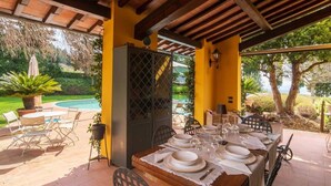 Um pátio externo com uma mesa de jantar posta para quatro pessoas, rodeado de cadeiras, e uma piscina ao fundo.