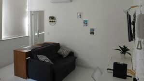 A modern living room with a black sofa, a wooden desk, and a white air conditioner on the wall. - Amazing, stylish 1-bedroom apartment in the heart of Copacabana! (Copacabana Rio de Janeiro)