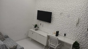 A modern bedroom with a flat-screen TV mounted on a textured wall, a white desk with a chair, and a patterned sofa. - Amazing, stylish 1-bedroom apartment in the heart of Copacabana! (Copacabana Rio de Janeiro)
