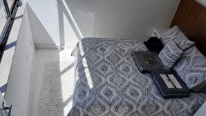 A small, modern room with a bed, a white fluffy rug, and a window with blinds. - Amazing, stylish 1-bedroom apartment in the heart of Copacabana! (Copacabana Rio de Janeiro)