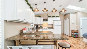 A modern kitchen with granite countertops, white cabinets, and pendant lighting. - Sunshine Hideaway - Team Joseph Ellen (Jacksonville Beach)
