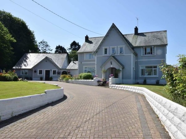 A large, two-story house with a paved driveway leading to a white-walled entrance.