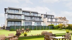 Un immeuble résidentiel moderne à plusieurs étages, doté de balcons, d’une pelouse bien entretenue et d’un espace extérieur aménagé pour s’asseoir.