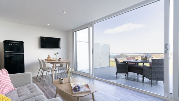 Un salon moderne doté d’un téléviseur à écran plat, d’un coin repas et d’un balcon offrant une vue sur la mer.