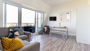 A spacious living area with a sofa, a dining table, and a TV mounted on the wall. - 7 Beachview - apartment in Crantock sleeps 4 guests in 2 bedrooms (Crantock)