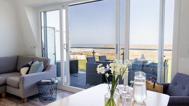 A modern living room with a large sliding glass door leading to a balcony with a view of the sea. - 7 Beachview - apartment in Crantock sleeps 4 guests in 2 bedrooms (Crantock)