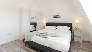 A modern bedroom with a bed, bedside tables, a wardrobe, and a painting on the wall. - 8 Beachview -  apartment in Crantock sleeps 4 guests in 1 bedroom (Crantock)