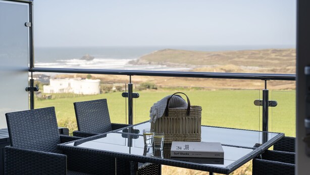 A balcony with a glass table, wicker chairs, and a view of the ocean. - 8 Beachview -  apartment in Crantock sleeps 4 guests in 1 bedroom (Crantock)