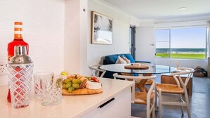 A modern kitchen with a glass table, a bottle of red wine, and a fruit platter. - Absolute Beachfront Apartment 3B (Lennox Head)