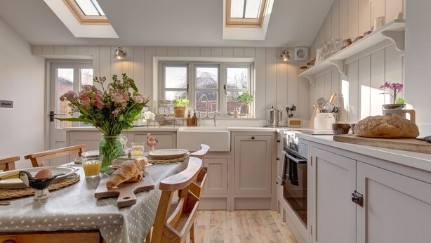 A kitchen with a dining table, chairs, a vase of flowers, and a window with a view. - The Flints - sleeps 3 guests  in 2 bedrooms (Langham)