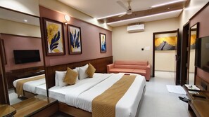 A hotel room with a bed, a sofa, a TV, and artwork on the walls. - Hotel Riddhi Executive (Latur)