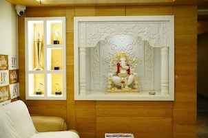 Um quarto com parede de painel de madeira, um nicho decorativo branco com a figura de uma divindade e uma estante com troféus.
