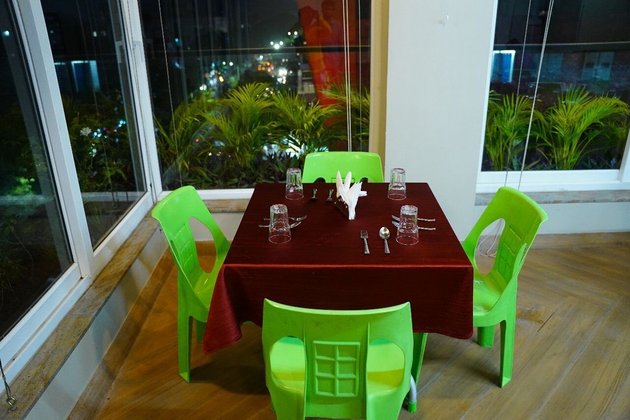 A dining area with a table set for four, green chairs, and a view of greenery outside.